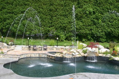 Diseño de piscina con fuente natural grande a medida en patio trasero con adoquines de hormigón