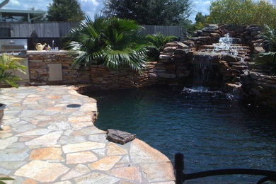 Ejemplo de piscina con fuente exótica grande a medida en patio trasero con adoquines de piedra natural