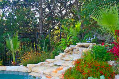 Large back natural swimming pool in Austin with a water feature and natural stone paving.