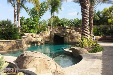 Large island style backyard stone and custom-shaped aboveground water slide photo in Orange County