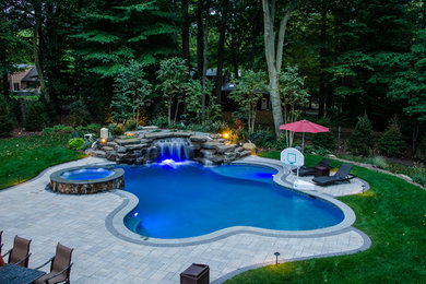 Foto de piscina con fuente natural clásica renovada grande a medida en patio trasero con adoquines de piedra natural