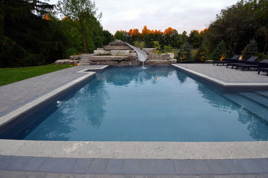 Diseño de piscina con tobogán alargada tradicional renovada de tamaño medio rectangular en patio trasero con adoquines de ladrillo