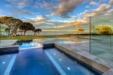 Cette photo montre une grande piscine à débordement et arrière sur mesure avec un point d'eau et des pavés en pierre naturelle.