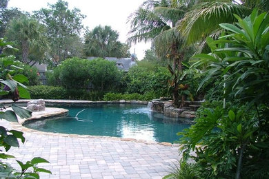 Ejemplo de piscina grande a medida en patio trasero con adoquines de hormigón
