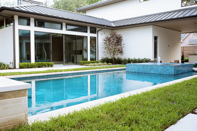 Modelo de piscina con fuente alargada actual de tamaño medio rectangular en patio trasero con losas de hormigón