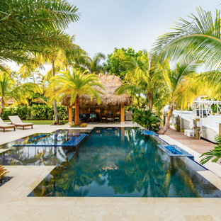Esempio di una piscina a sfioro infinito tropicale rettangolare di medie dimensioni e dietro casa con pavimentazioni in pietra naturale e una vasca idromassaggio