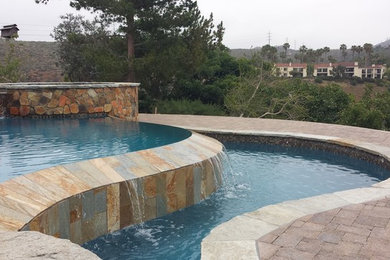 Foto de piscina con fuente elevada tradicional grande a medida en patio trasero con adoquines de piedra natural