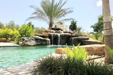 Ejemplo de piscina con fuente natural tropical grande a medida en patio trasero con adoquines de piedra natural