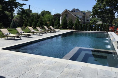 Diseño de piscina con fuente tradicional grande rectangular en patio trasero con adoquines de hormigón