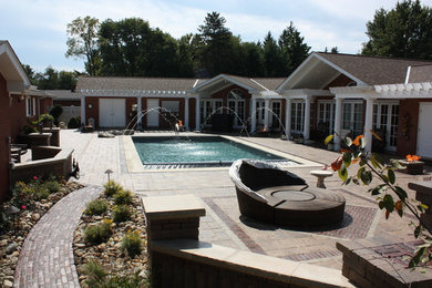 Modelo de piscina alargada clásica renovada de tamaño medio rectangular en patio trasero con adoquines de hormigón