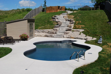Imagen de piscina tradicional de tamaño medio a medida en patio trasero con losas de hormigón