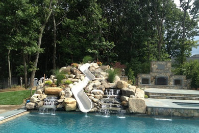 Diseño de piscina con tobogán alargada contemporánea grande rectangular en patio trasero con adoquines de piedra natural