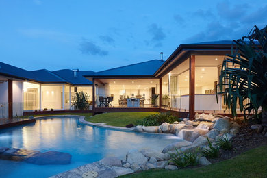Imagen de piscina infinita tropical grande a medida en patio trasero con adoquines de piedra natural