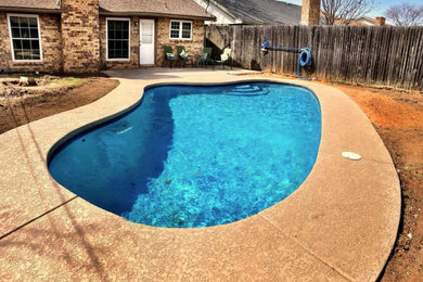 Modelo de piscina natural actual de tamaño medio tipo riñón en patio trasero con suelo de hormigón estampado