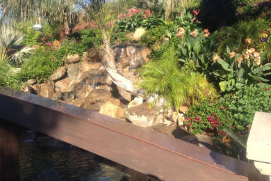 Large island style backyard stone and kidney-shaped water slide photo in Los Angeles
