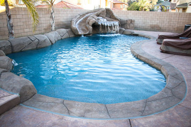 Imagen de piscina con tobogán exótica de tamaño medio a medida en patio trasero con suelo de hormigón estampado