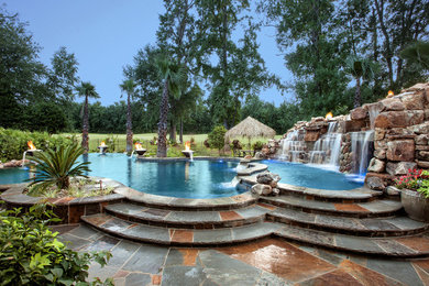 Huge island style backyard stone and custom-shaped infinity hot tub photo in New Orleans