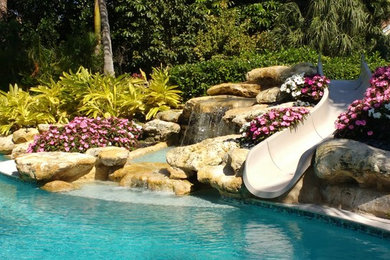 Water slide - large coastal backyard stone and rectangular infinity water slide idea in Miami