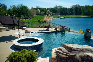 Foto di un'ampia piscina a sfioro infinito classica personalizzata dietro casa con un acquascivolo e pavimentazioni in pietra naturale