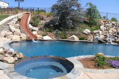 Modelo de piscina con tobogán clásica de tamaño medio tipo riñón en patio trasero con adoquines de piedra natural