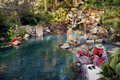 Ejemplo de piscina con tobogán natural exótica grande a medida en patio trasero con adoquines de piedra natural