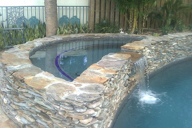 Example of a mid-sized tuscan backyard stone and round hot tub design in Miami