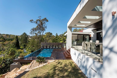 Réalisation d'un grand couloir de nage arrière minimaliste rectangle avec une terrasse en bois.