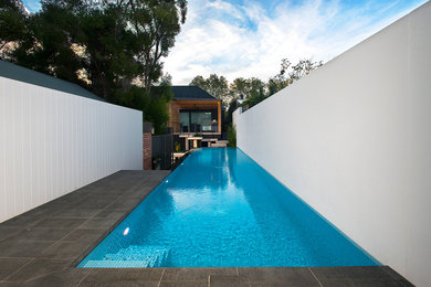 Medium sized modern back rectangular infinity swimming pool in Adelaide with natural stone paving.