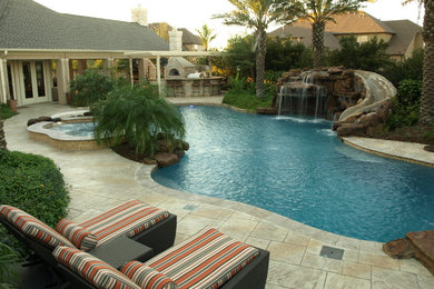 Modelo de piscina con tobogán alargada tropical grande a medida en patio trasero con suelo de baldosas