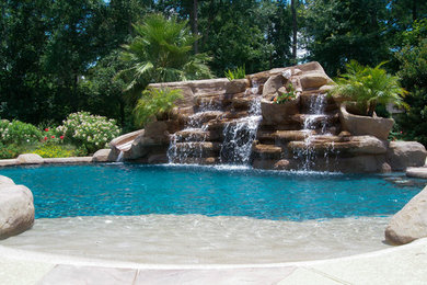 Ejemplo de piscina con tobogán natural tropical de tamaño medio a medida en patio trasero con suelo de hormigón estampado