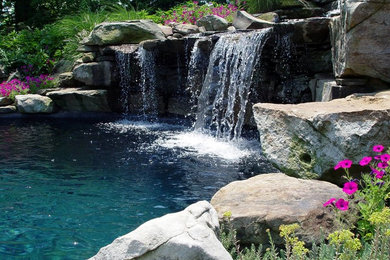 Ejemplo de piscina con fuente alargada clásica grande a medida en patio trasero con adoquines de piedra natural