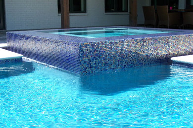 Ispirazione per una piscina contemporanea a "L" di medie dimensioni e dietro casa con una vasca idromassaggio e lastre di cemento