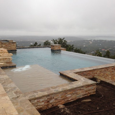 Mid-sized tuscan backyard concrete paver and rectangular infinity hot tub photo in Austin