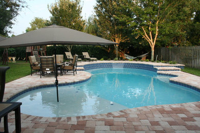 Diseño de piscina con fuente alargada tradicional de tamaño medio a medida en patio trasero con adoquines de ladrillo
