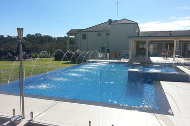 Expansive modern back rectangular infinity swimming pool in Sydney with concrete paving and a pool house.