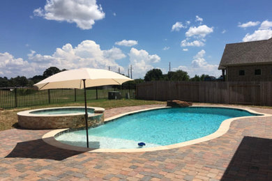 Mid-sized elegant backyard brick and custom-shaped hot tub photo in Houston