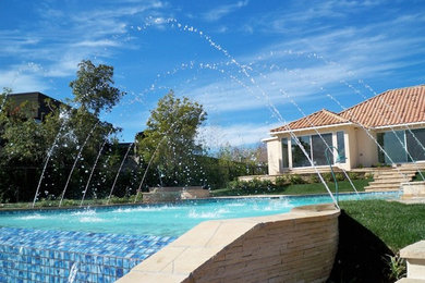 Ejemplo de piscinas y jacuzzis alargados tradicionales de tamaño medio a medida en patio trasero con adoquines de piedra natural
