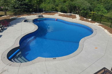 Diseño de piscina natural grande a medida en patio trasero con suelo de hormigón estampado