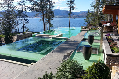 Modelo de piscinas y jacuzzis infinitos actuales extra grandes rectangulares en patio trasero con adoquines de piedra natural