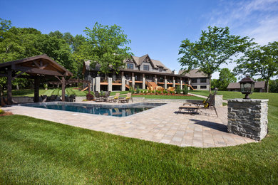 Modelo de piscina alargada rural grande en forma de L en patio trasero con adoquines de hormigón