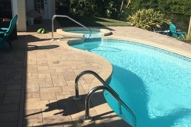 Diseño de piscinas y jacuzzis alargados tropicales pequeños tipo riñón en patio trasero con adoquines de ladrillo