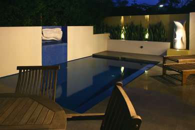 Diseño de piscina con fuente alargada contemporánea de tamaño medio rectangular en patio trasero con adoquines de hormigón