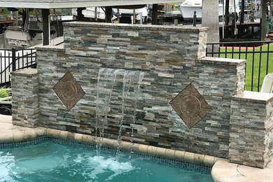 Imagen de piscina con fuente alargada tradicional grande a medida en patio trasero con adoquines de piedra natural