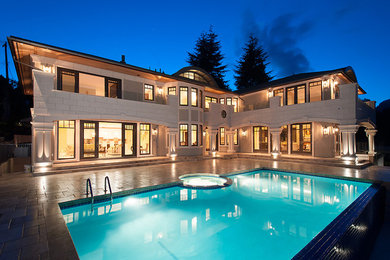 Diseño de piscina infinita clásica grande rectangular en patio trasero con adoquines de piedra natural