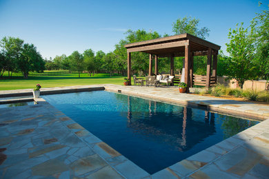 Modelo de piscina natural clásica grande rectangular en patio trasero con adoquines de piedra natural