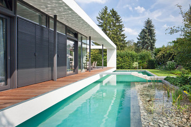 Großer Moderner Schwimmteich neben dem Haus in individueller Form mit Wasserspiel und Dielen in Berlin