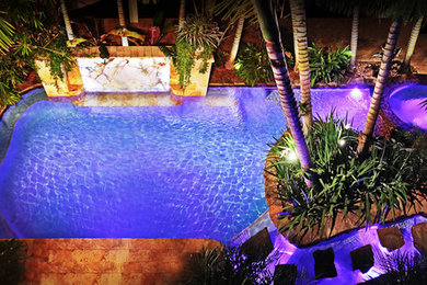 Idee per una grande piscina naturale tropicale rettangolare dietro casa con pavimentazioni in pietra naturale e una dépendance a bordo piscina