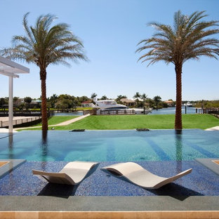 Foto di un'ampia piscina a sfioro infinito tropicale rettangolare dietro casa con piastrelle