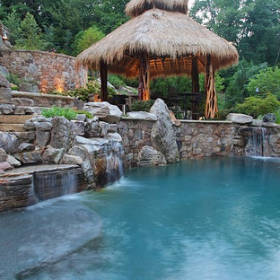 Ejemplo de piscina con fuente tropical, grande, en patio trasero