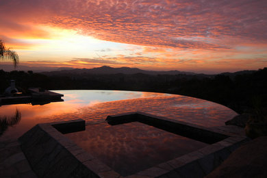 Ispirazione per una grande piscina a sfioro infinito design personalizzata dietro casa con pavimentazioni in pietra naturale